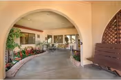 A covered arched interior walkway with potted plants, seating, and a wooden bench swing under a stucco ceiling.