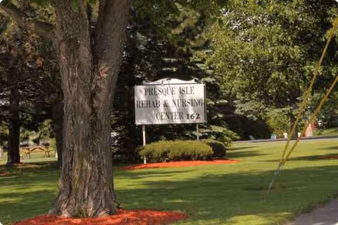 Outdoor scene with a sign reading Presque Isle Rehab & Nursing Center on a grassy lawn.