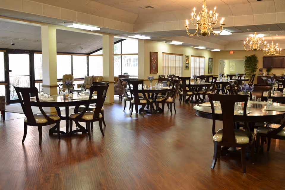 Spacious dining room with round wooden tables and chairs, chandeliers, and place settings.