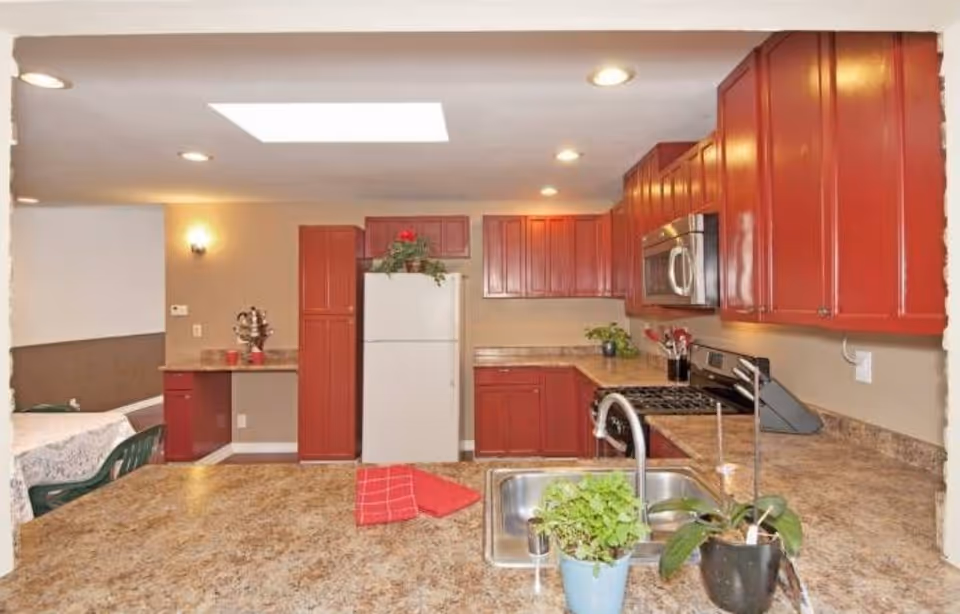 Red kitchen cabinets surround a spacious kitchen with stainless steel appliances and sink.