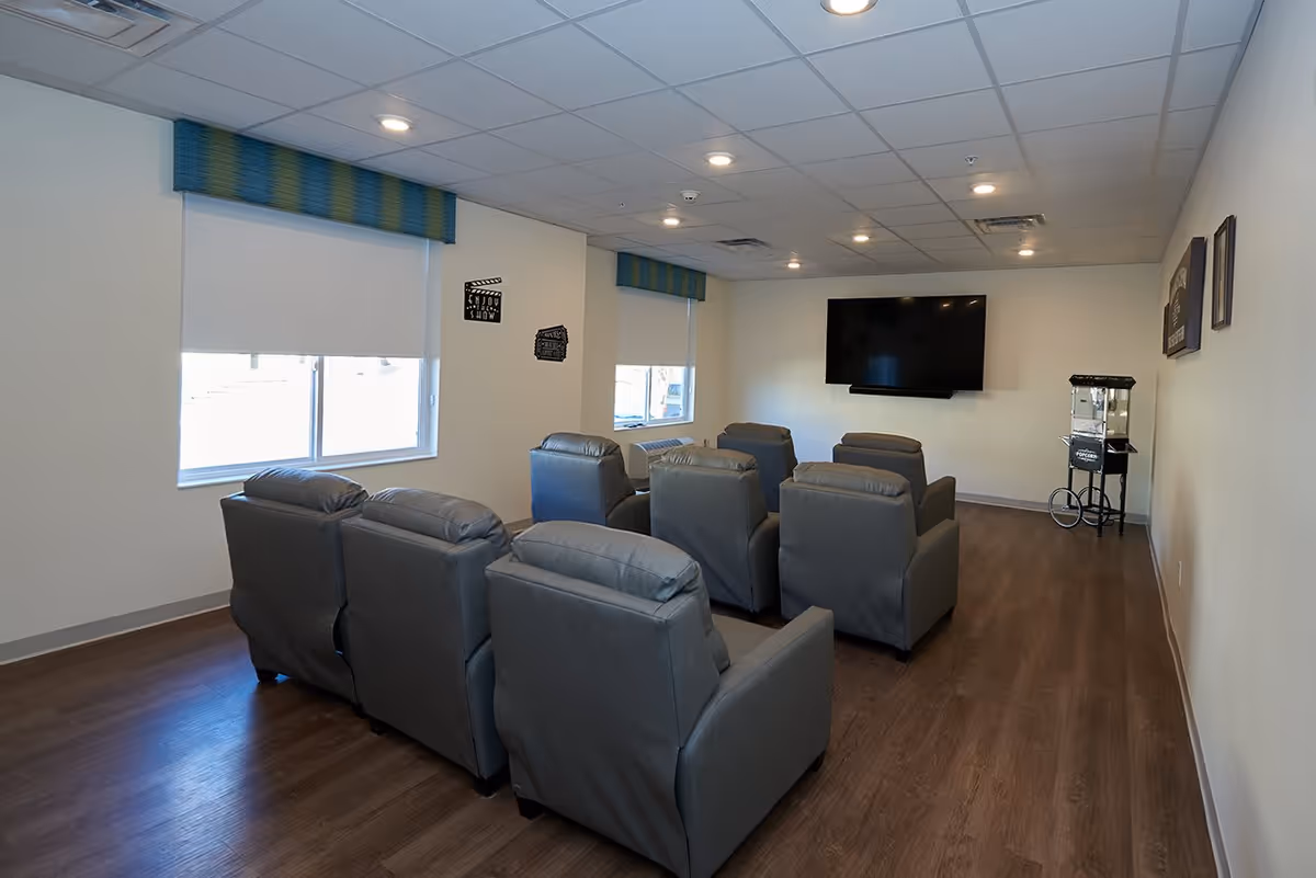Small media room with two rows of gray recliners facing a wall-mounted TV and a popcorn machine.