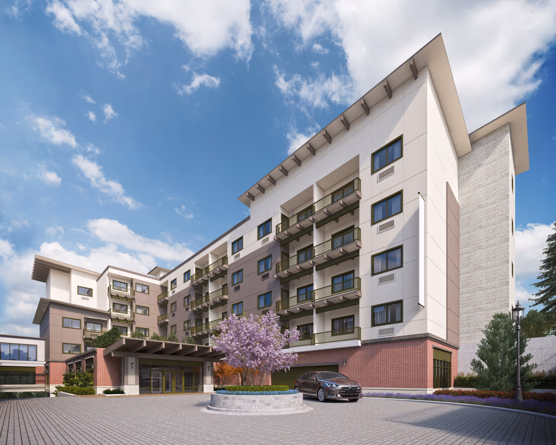 Exterior view of a multi-story assisted living building showing the main entrance canopy, a parked car, and a landscaped roundabout with a blooming tree.