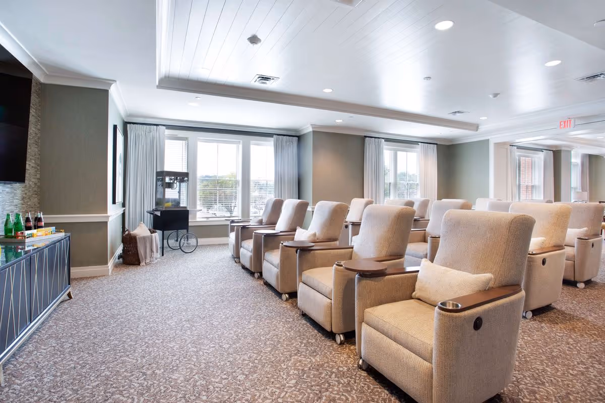 Spacious bright common room with rows of beige recliner chairs, small side trays, and large windows.