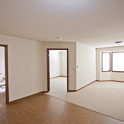 Empty apartment interior showing wood and carpeted floors, an open doorway, and a bay window.