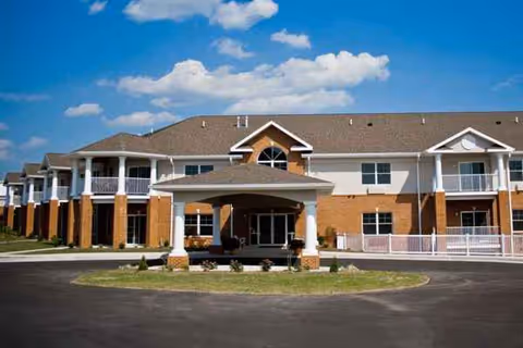 Exterior view of a two-story senior living facility with brick columns and a circular driveway.