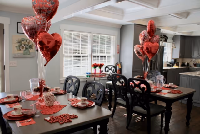 Dining area decorated for Valentine's Day with tables set with red heart-themed tableware and balloons.