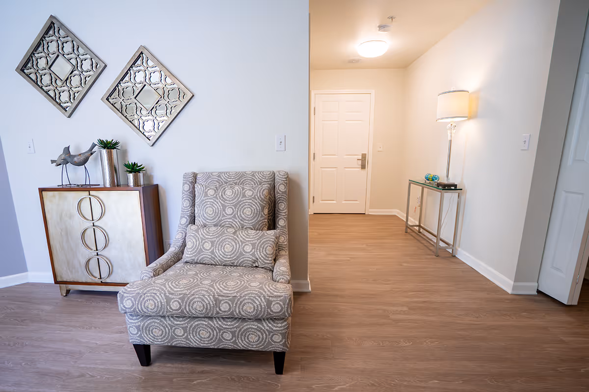 Stylish entry and seating area with a patterned armchair, decorative cabinet and mirrors, and a hallway leading to a closed front door.