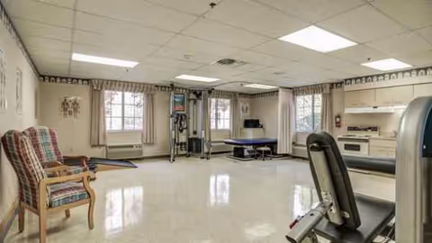 Spacious interior therapy room with exercise equipment, a bed, and kitchenette area.