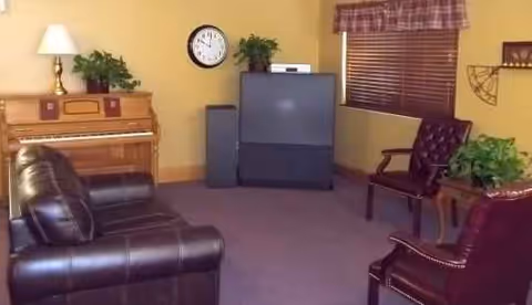 Living room with a leather sofa, chairs, piano, clock, TV, and plants.