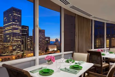 Indoor dining area with tables set for meals and a city skyline view.
