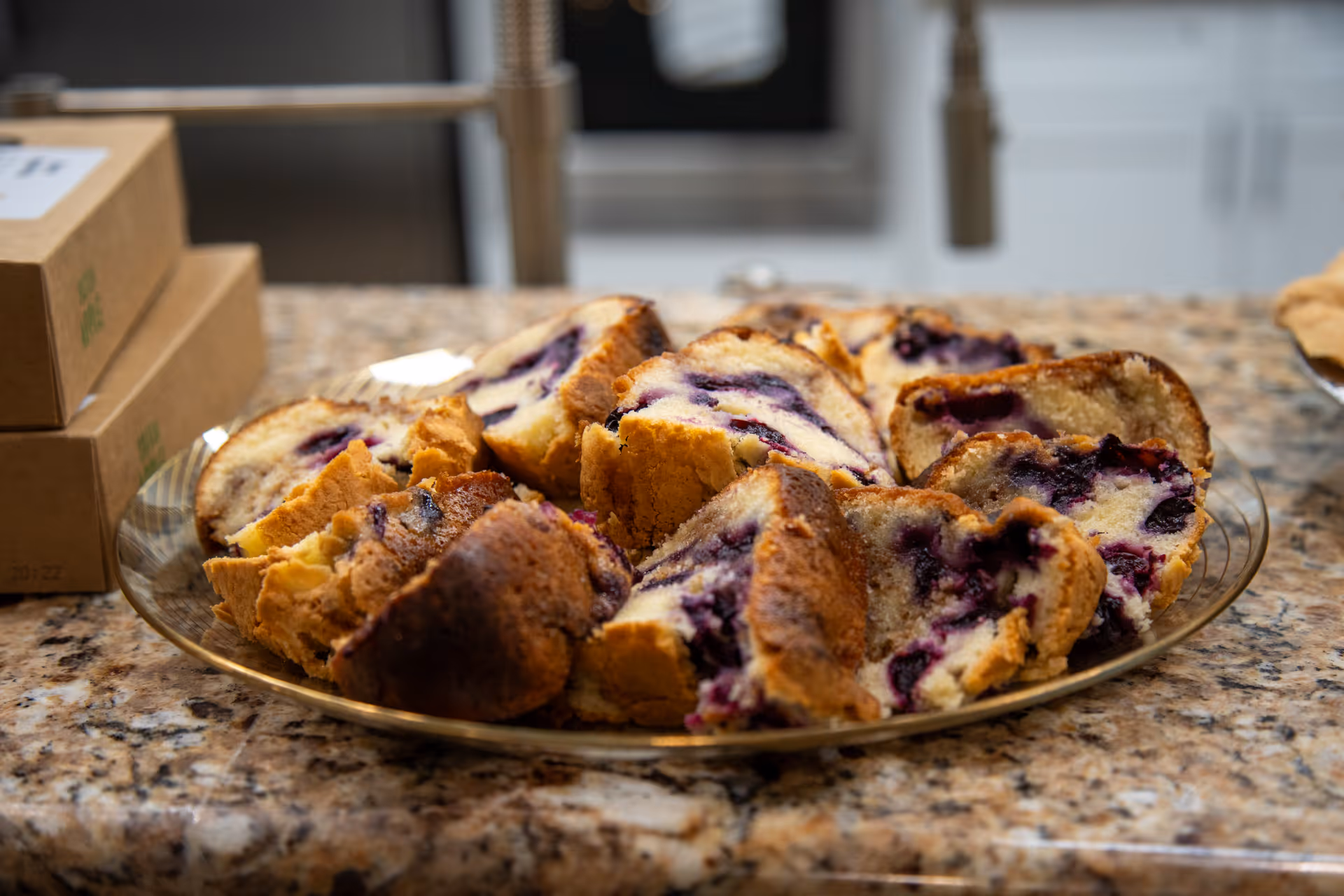 A plate of sliced blueberry loaf cake on a granite kitchen countertop with a sink and cabinets in the background.