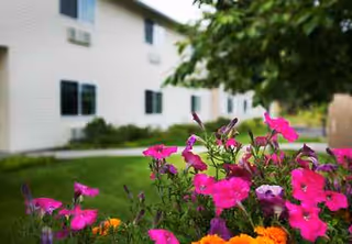 Exterior view of a white senior living building with colorful flowers in foreground.