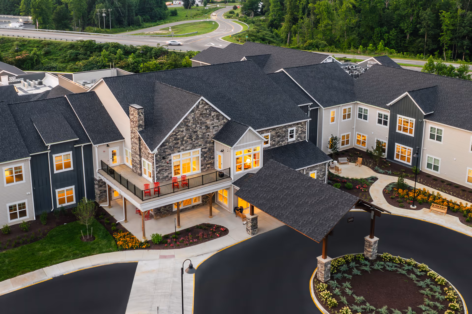 Aerial view of the senior living building showing a stone-clad entrance, covered porte-cochère, balcony with chairs, and landscaped circular driveway.