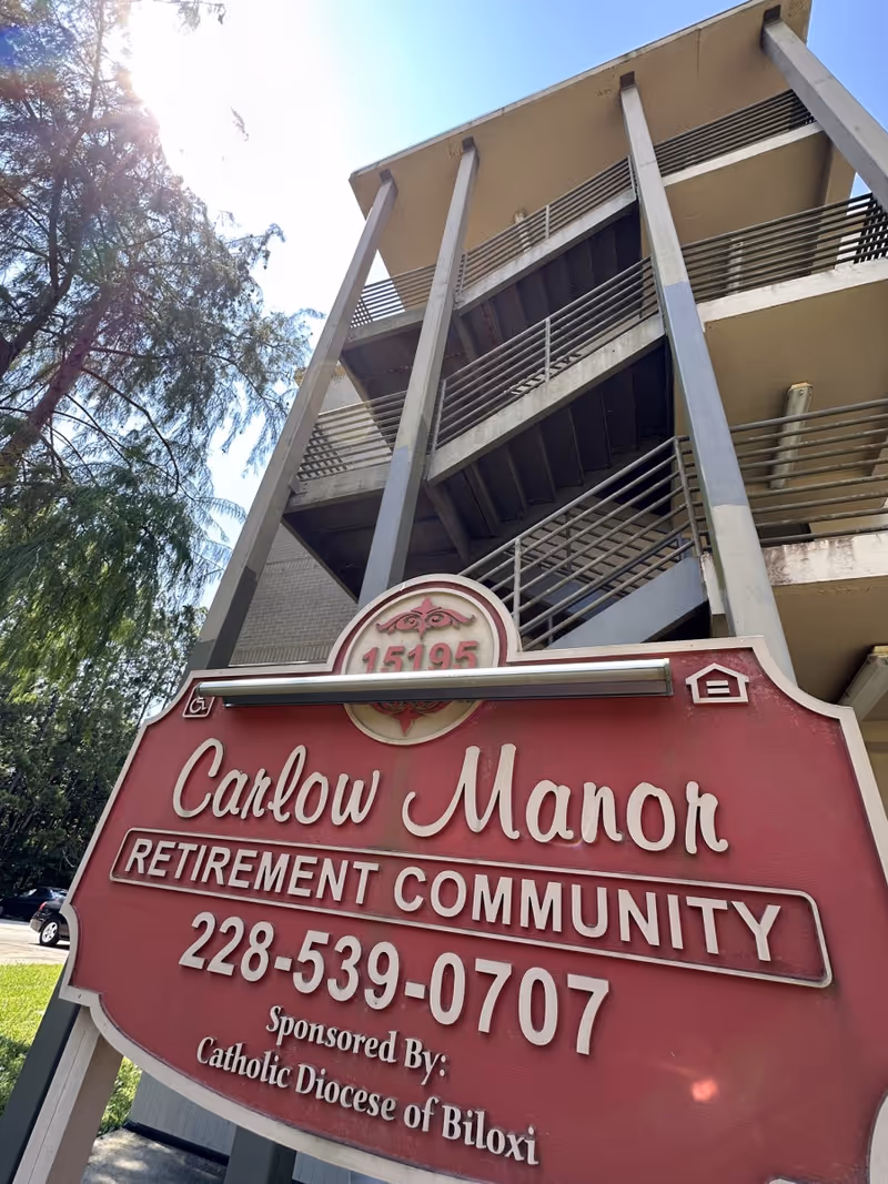 Exterior view of Carlow Manor Retirement Community featuring a tall stairwell and a red front sign.