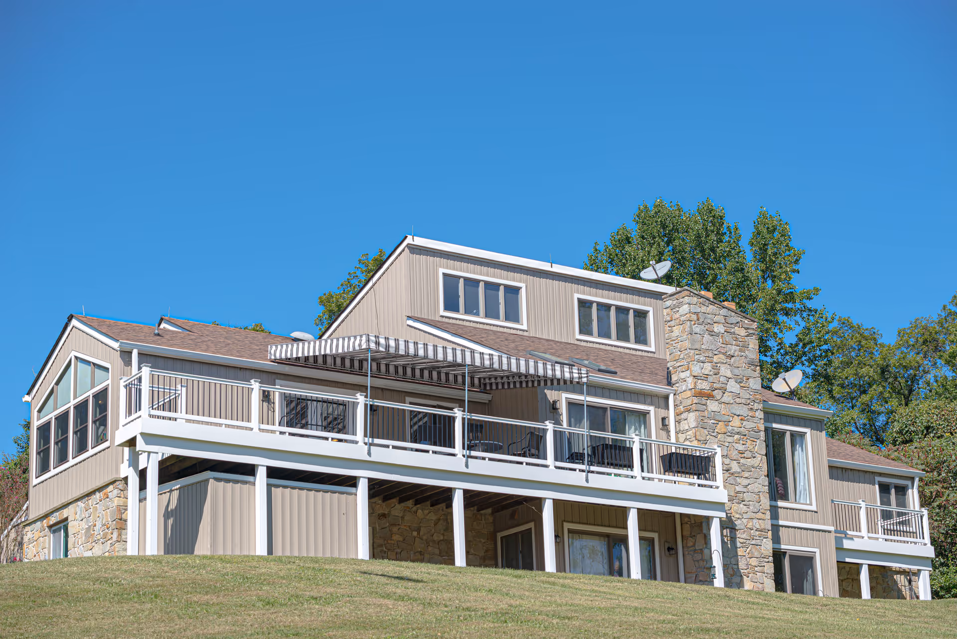 Exterior front of a multi-level building with balconies, a stone chimney, and a striped awning under a clear blue sky.