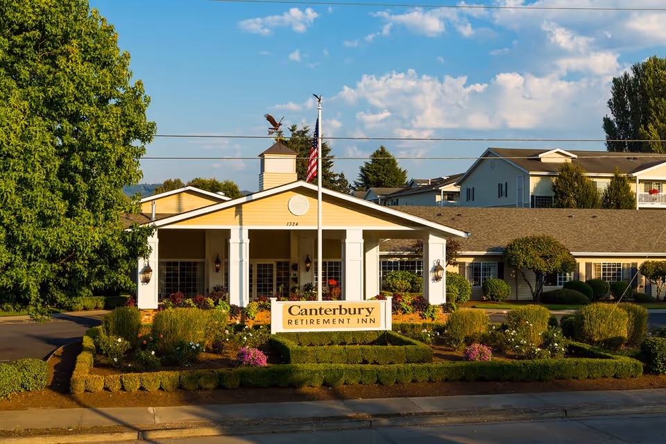 Front entrance of Canterbury Retirement Inn with landscaped gardens, a flagpole, and the building facade.