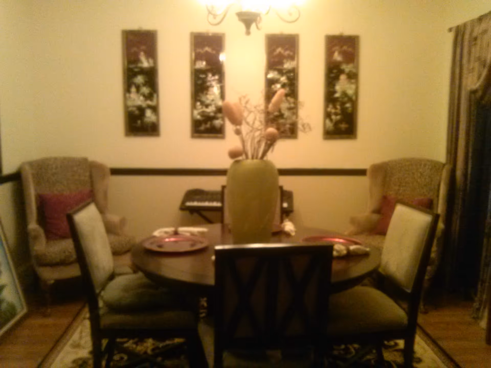 Warmly lit dining room with a round table, vase centerpiece, upholstered chairs and wall art on the back wall.