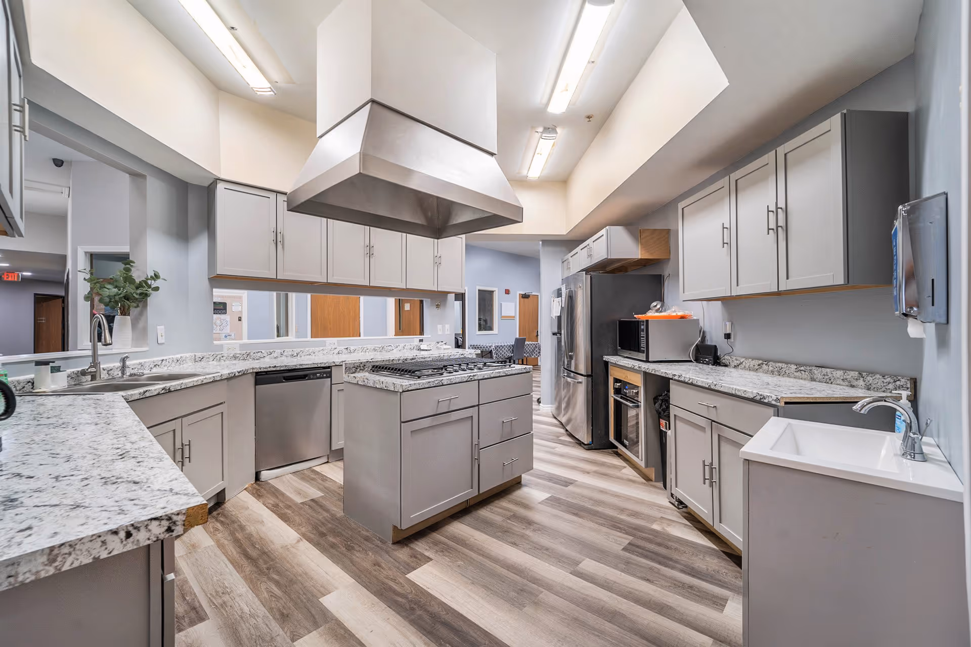Spacious modern communal kitchen with a central island, stainless steel appliances, gray cabinets and marble-patterned countertops.