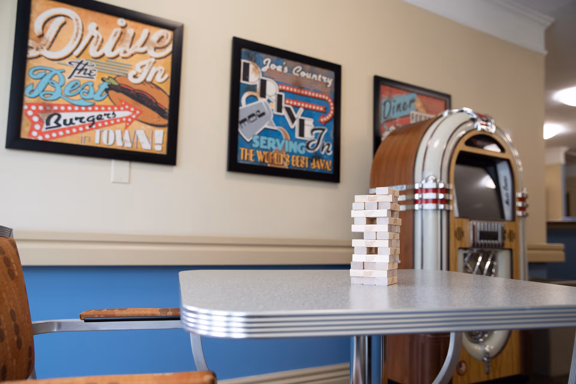 Retro-styled common area with a table holding a stack of Jenga blocks, a jukebox and framed diner-themed artwork on the wall.