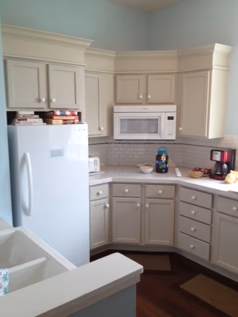 Bright kitchen with white cabinets, refrigerator, microwave, and countertop appliances.