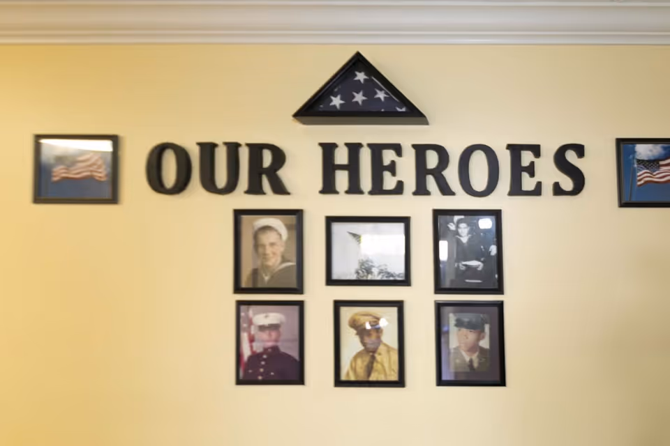 A wall display with the words 'OUR HEROES' in large black letters, surrounded by framed photographs of military personnel and two framed American flags. A folded American flag in a triangular display case is mounted above the text.