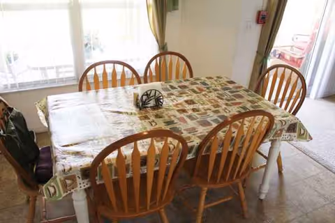 Dining table with six wooden chairs by a sunlit window in a bright room