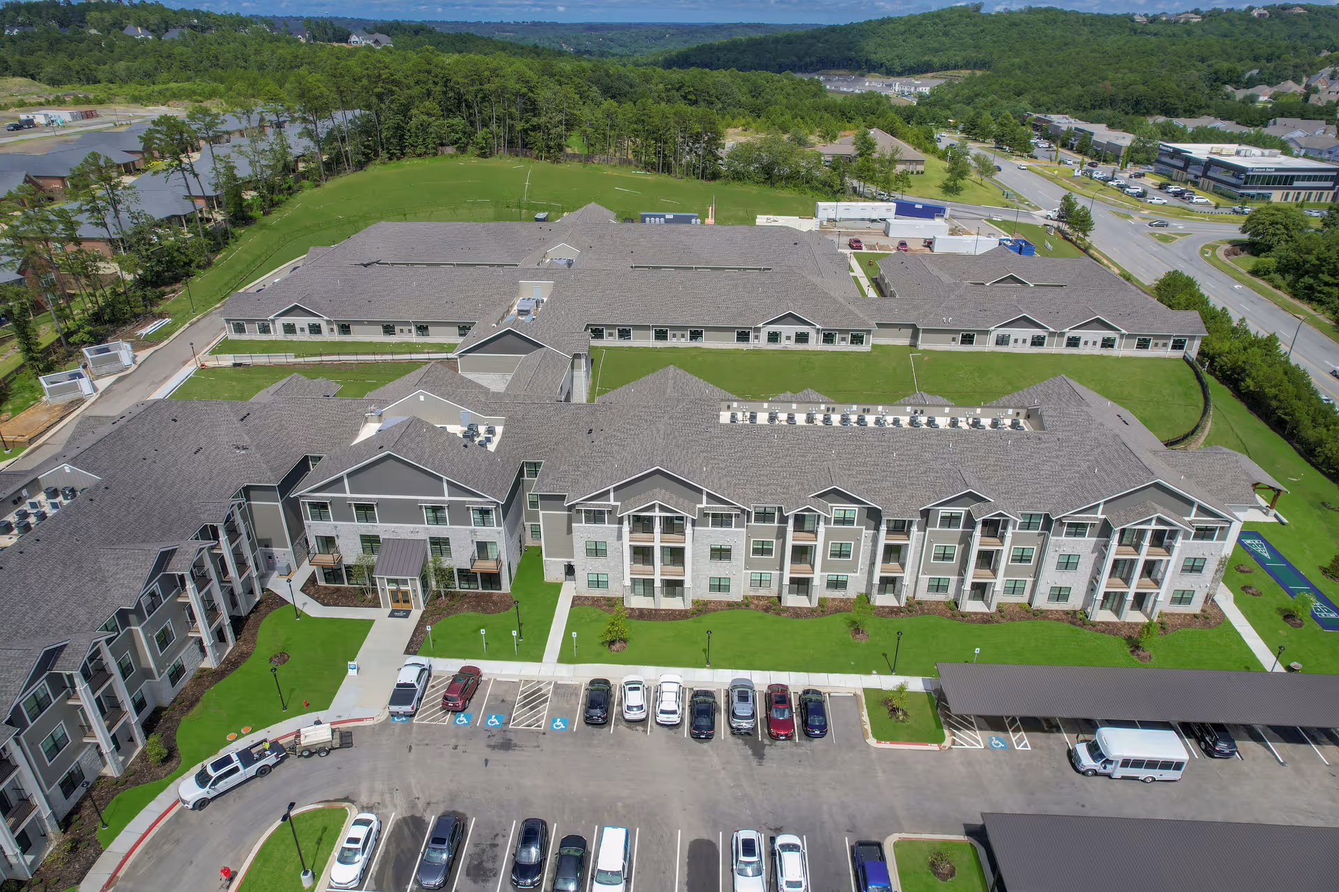 Aerial view of a large multi-building retirement community with landscaped lawns, parking lot, and surrounding roads and trees.