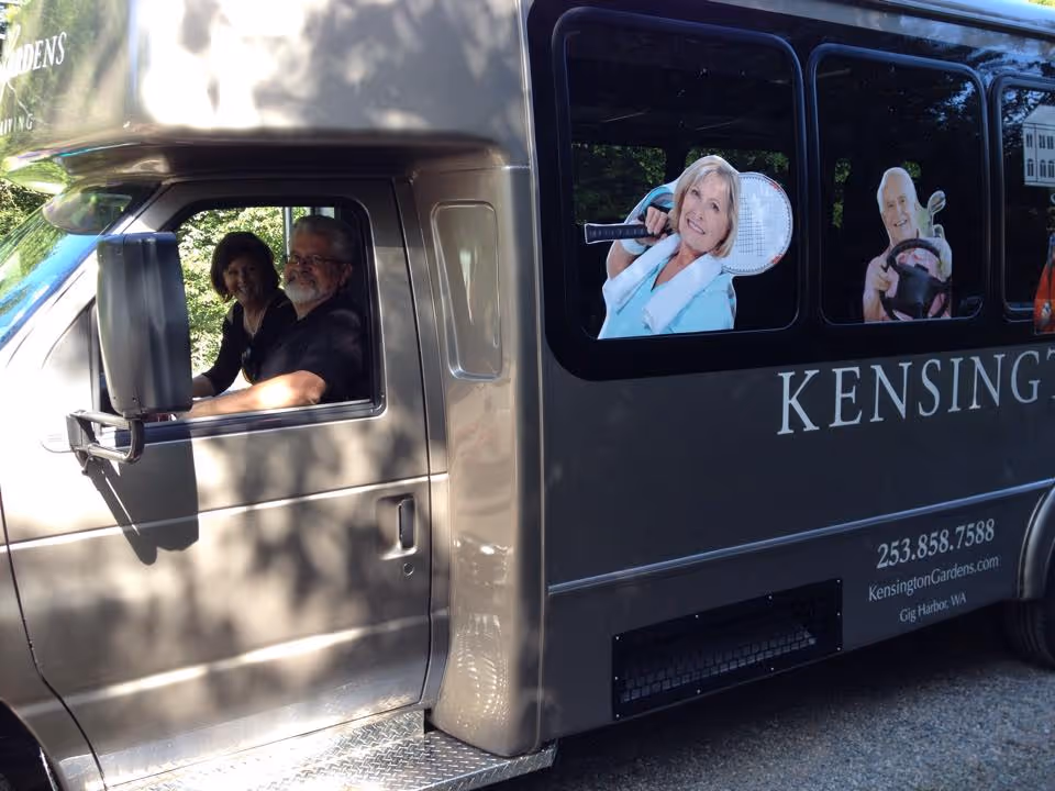 A Kensington Gardens shuttle bus parked outside with two people in the driver's cab and promotional images and the KensingtonGardens.com URL on the side.
