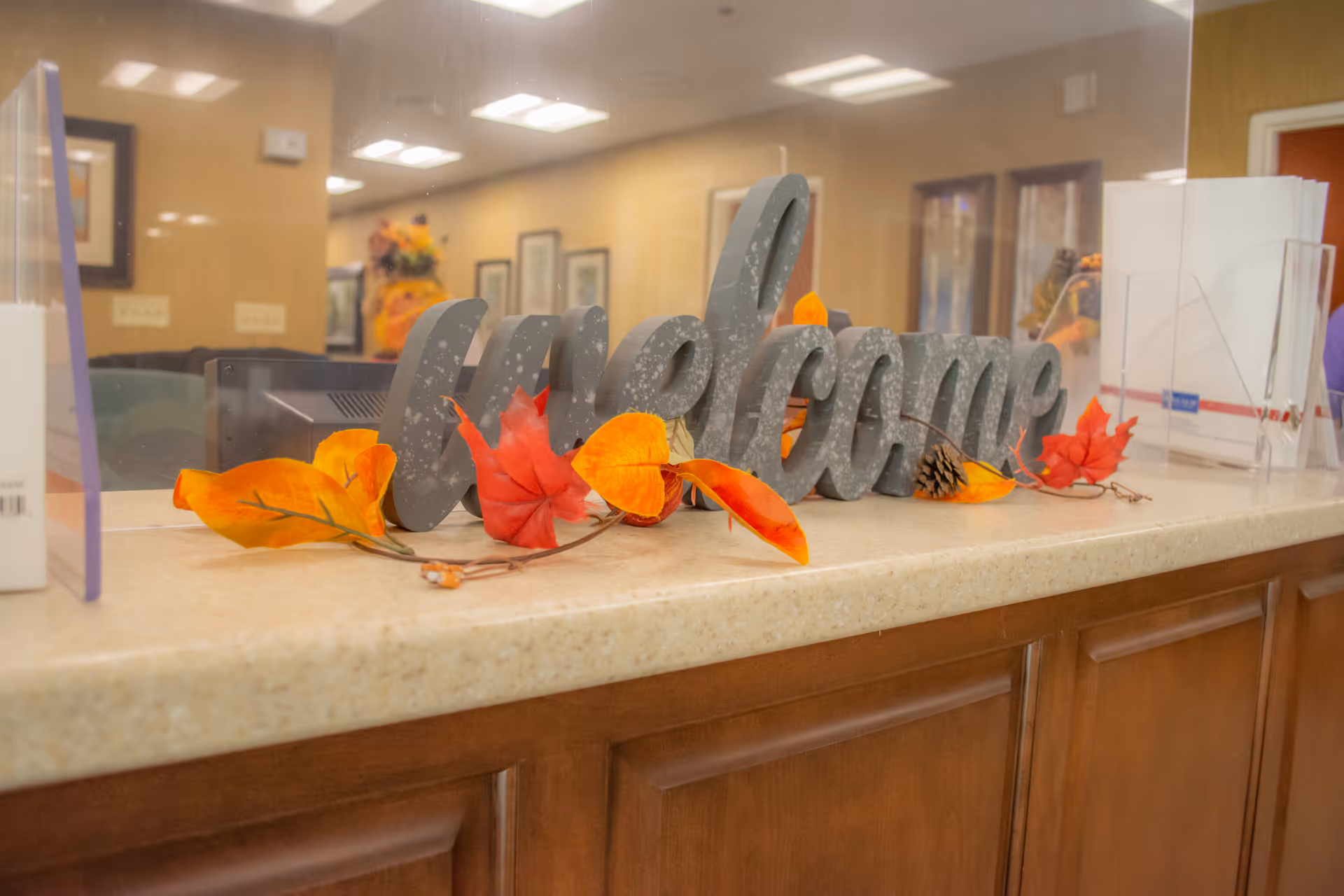A reception desk with a decorative 'welcome' sign and autumn leaf decorations behind a clear protective screen.