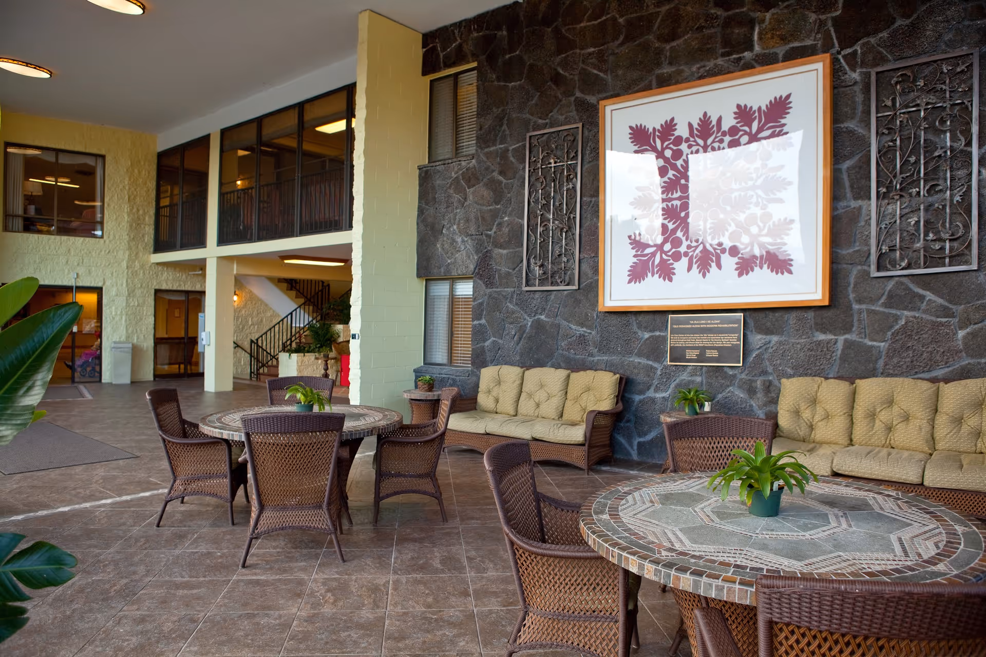 Lobby seating area with wicker tables and chairs, cushioned sofas, and a large framed artwork on a stone wall.