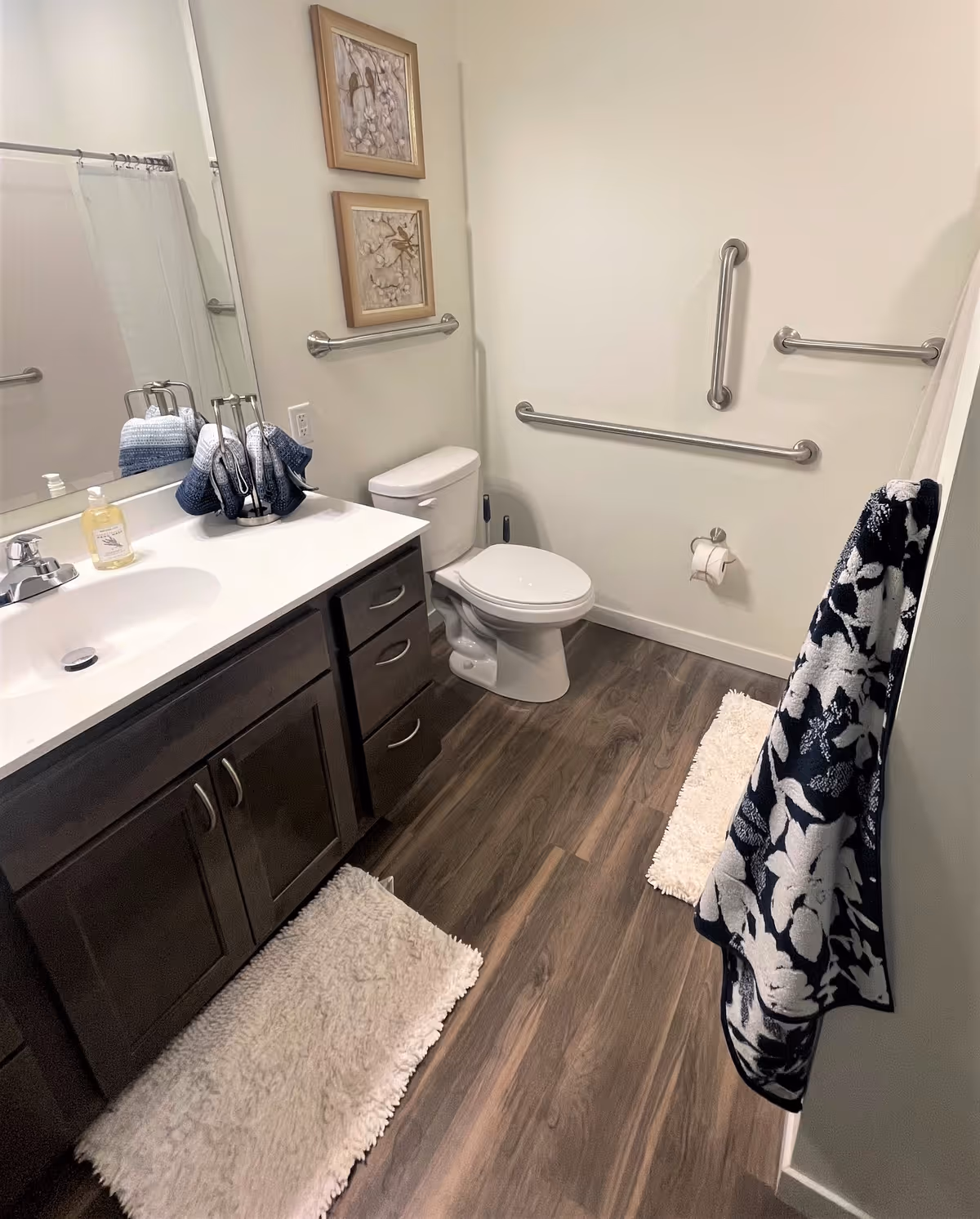 Accessible bathroom with a sink and vanity, toilet, multiple wall grab bars, and towels.
