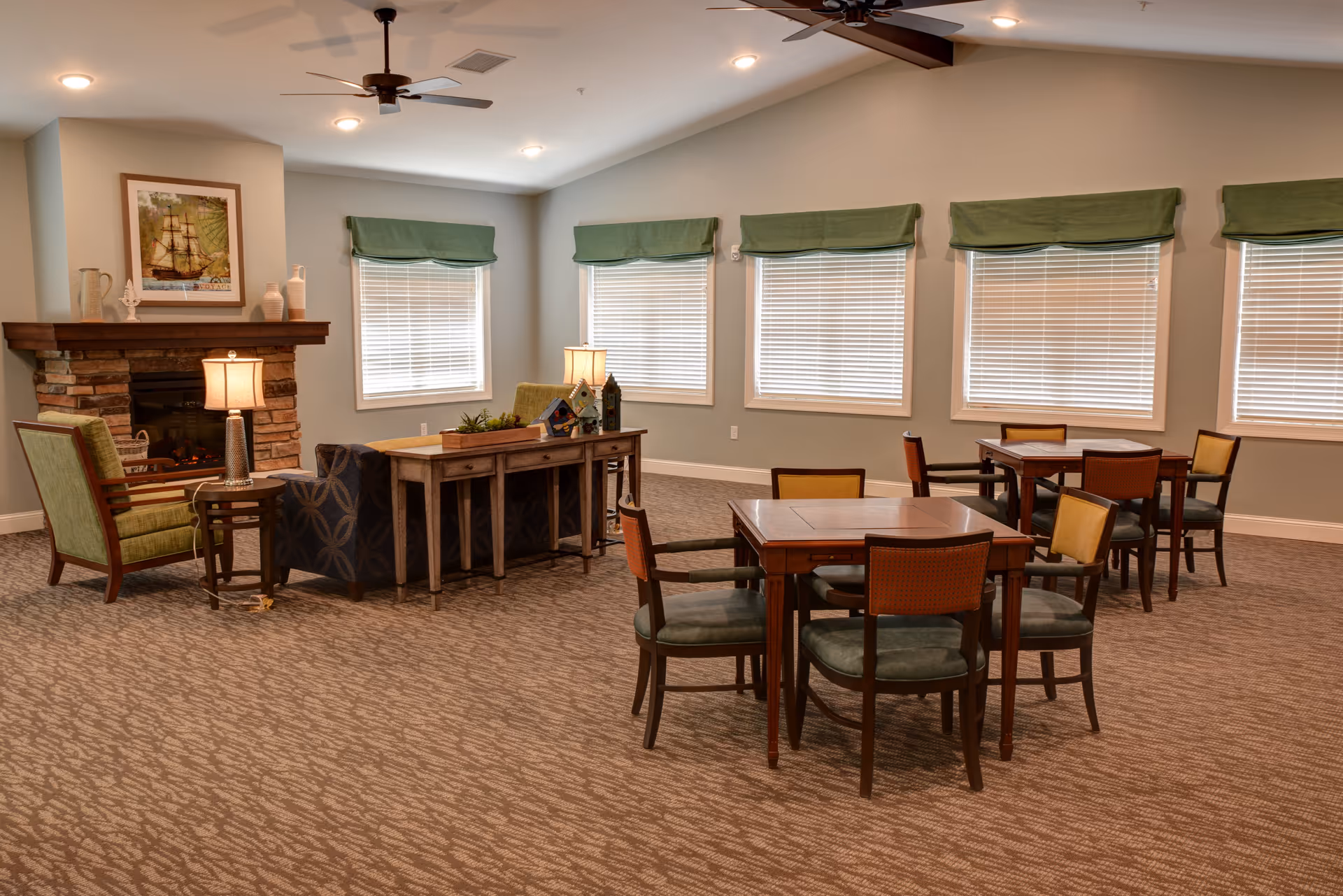 Well-lit common room with tables and chairs, lounge seating, and a stone fireplace.