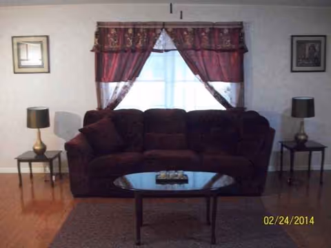 A burgundy sofa with end tables and lamps sits in a living room by curtained windows.
