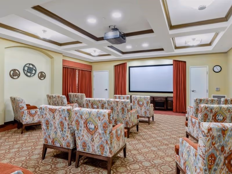 Small screening room with patterned armchairs arranged facing a projection screen and ceiling-mounted projector.