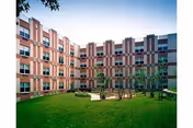 Courtyard with a green lawn, benches, and small trees surrounded by a multi-story brick residential building.