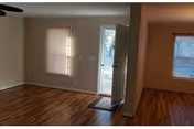 Empty interior living area with hardwood floors, an open front door, and windows with blinds.
