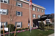 Brick senior living facility with flagpole, entrance canopy, and landscaped front lawn.
