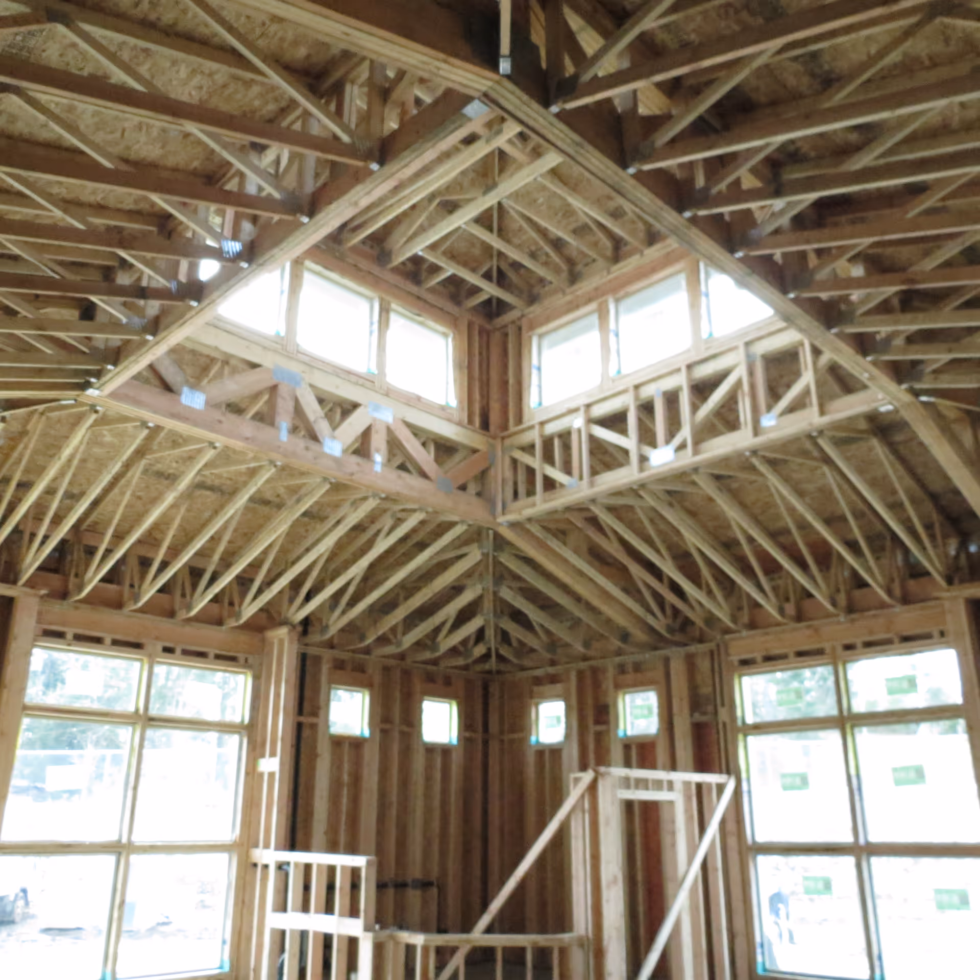 Interior view of a building under construction with exposed wooden studs, roof trusses, and windows.