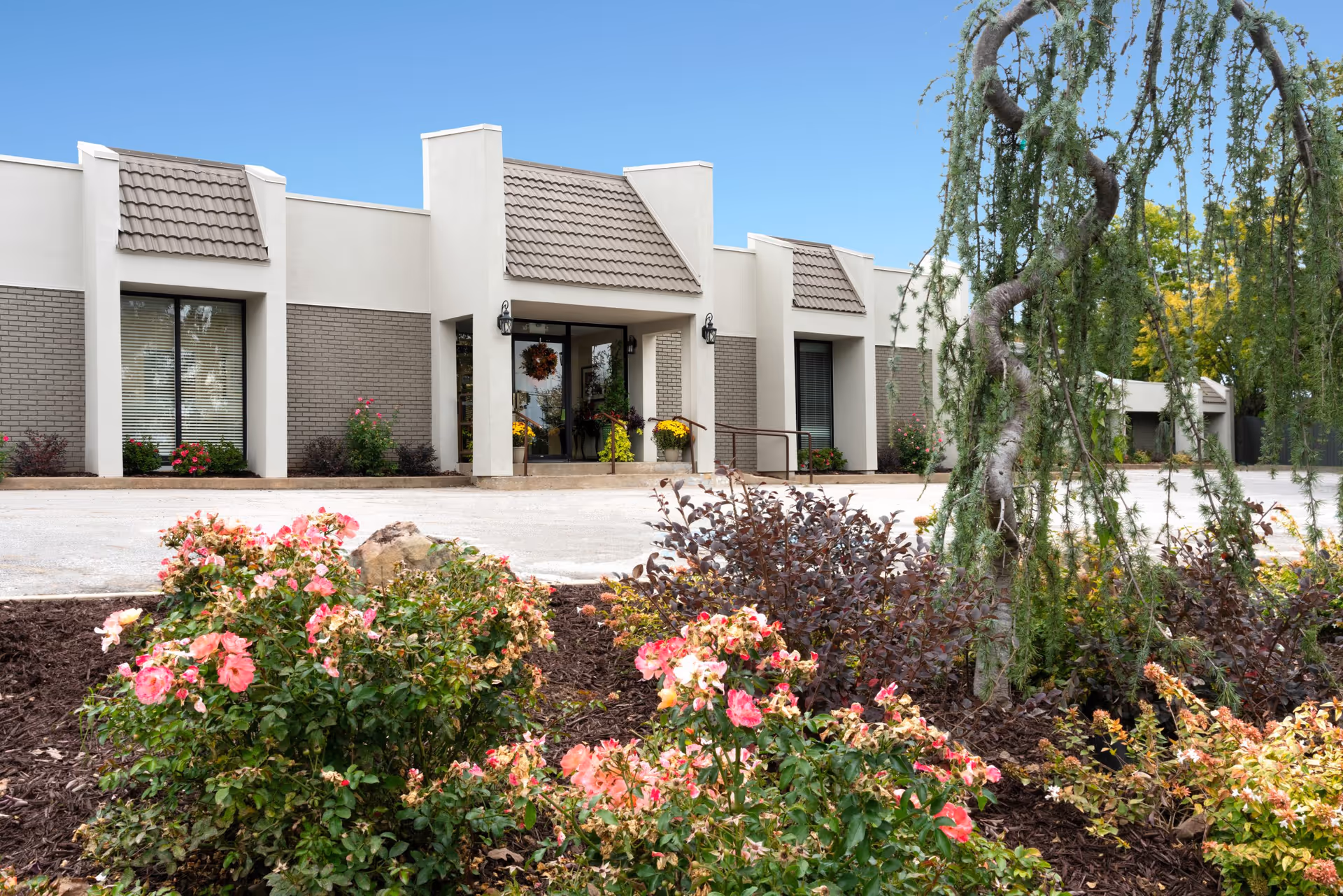 Front entrance of a single-story facility with a driveway and landscaped flower beds in front.