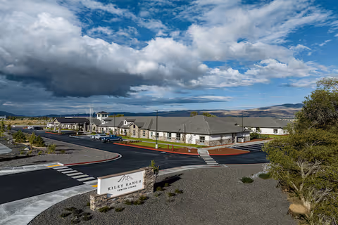 Aerial view of the Kiley Ranch Senior Living building, entrance sign, parking area and surrounding landscape under a dramatic cloudy sky.