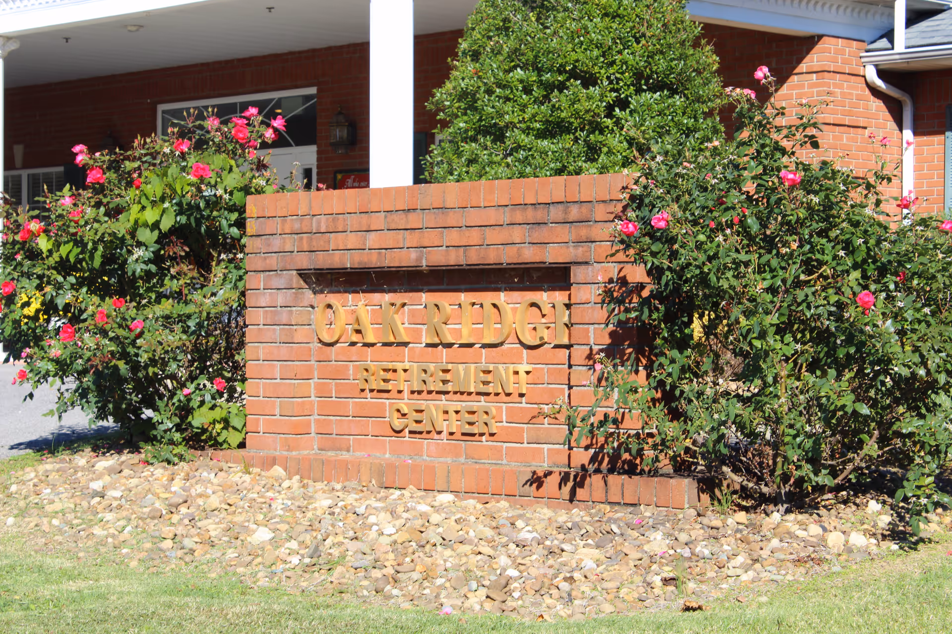 Brick entrance sign reading 'OAK RIDGE RETIREMENT CENTER' surrounded by flowering bushes in front of a brick building.