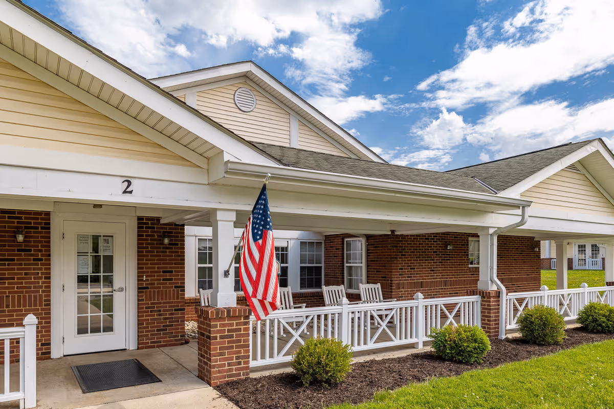 Front entrance of a brick cottage with a covered porch, rocking chairs, an American flag, and the number 2 above the door.