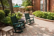 Outdoor brick courtyard with green rocking chairs, a small table, and umbrellas.