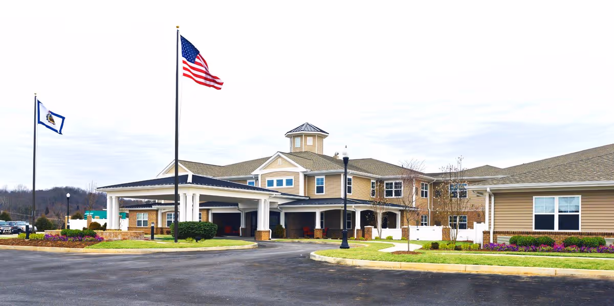 Front exterior of a senior living facility with a covered entrance, two flagpoles (one with an American flag), and landscaped grounds.