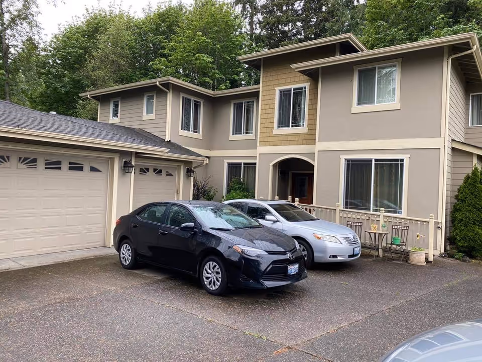 Front exterior of a two-story residential building with a three-car garage and two cars parked in the driveway.