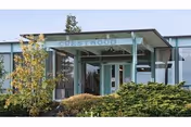 Exterior view of Crestwood Health and Rehab building entrance with a covered porch, surrounded by shrubs and trees under a clear sky.