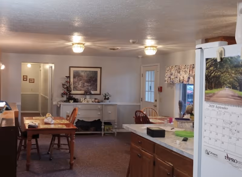 Cozy senior living dining area with wooden tables, chairs, a sideboard, and a calendar.