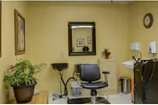 Small salon-style room with a barber chair, mirror, sink and potted plants against yellow walls.