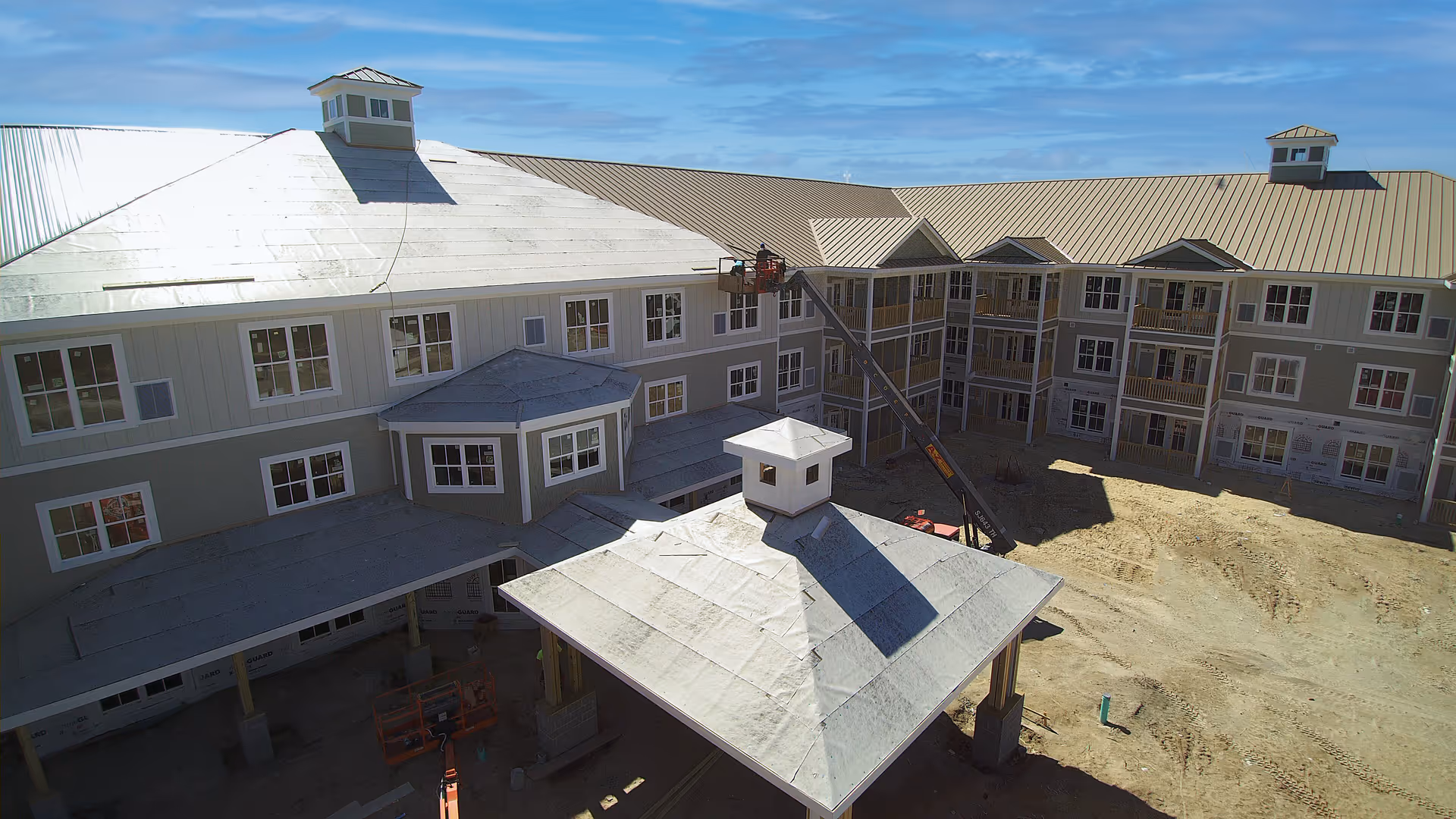 Aerial view of a multi-story senior living building under construction showing a central covered entrance, courtyard, and a construction lift.