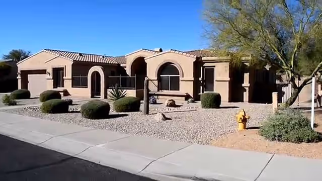 Single-story tan assisted living building with arched entryways and desert landscaping in front.